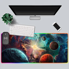 Top-down white desk setup with the Exoplanets RGB deskmat, keyboard, monitor, phone, and plant.